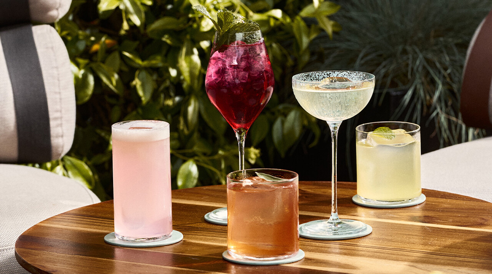 Five colourful cocktails on a wooden outdoor table