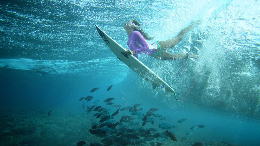 underwater shot of a girl diving beneath a wave with a surfboard