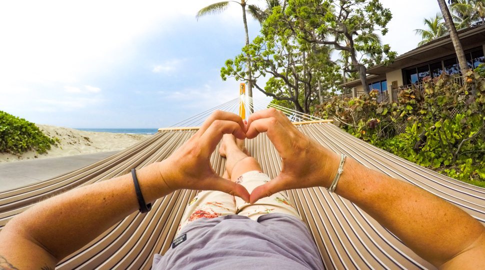 A person making a heart shape with their hands while in a hammock