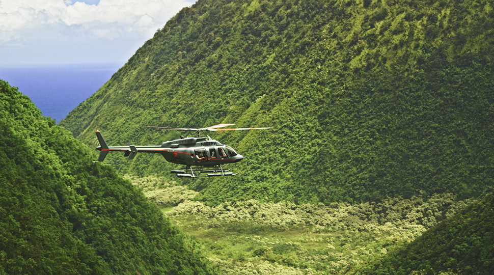 A helicopter flies over green peaks in Maui