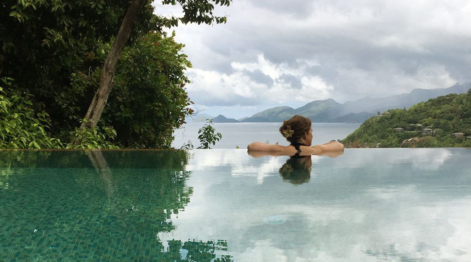A woman with a flower in her hair in a plunge pool with a view of the Indian Ocean