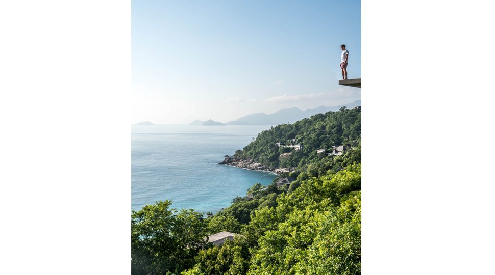 Robert Michael Poole stands on a ledge at Four Seasons Seychelles