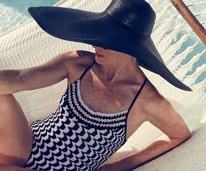 Woman in a black and white abstract print swimsuit and large black sunhat lounges in a hammock