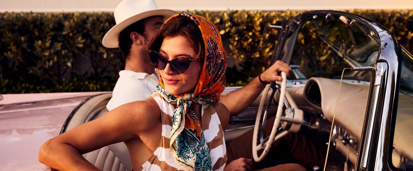A woman in a scarf and a man in a hat in an old vintage car