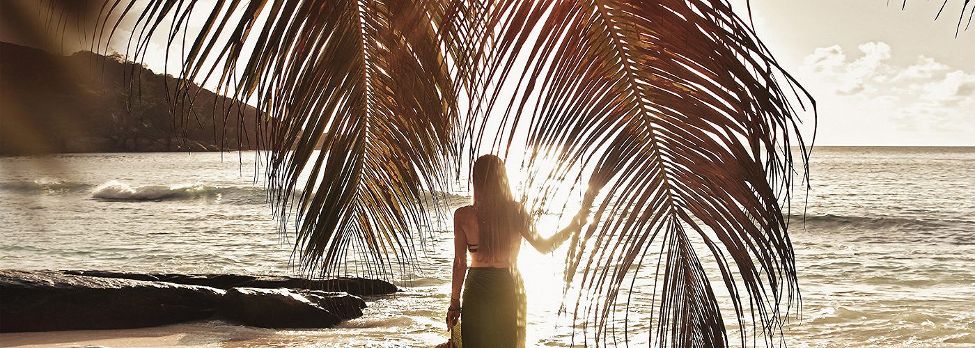 Woman standing between palm leaves on the beach