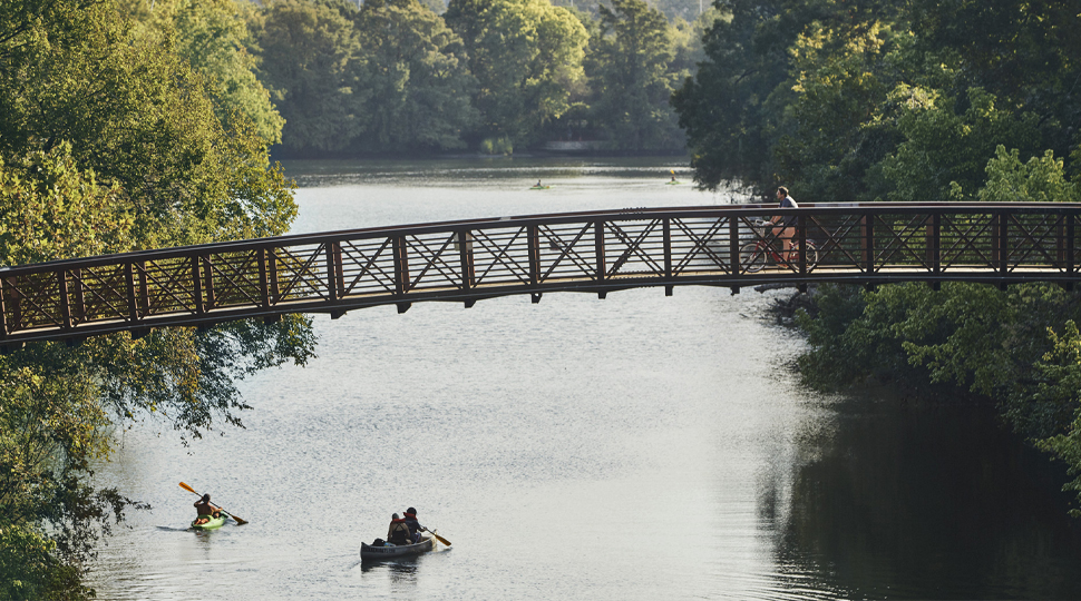 Pedestrian bridge crossing over Lady Bird Lake in Austin, Texas, with trees on either side and kayaks in the water