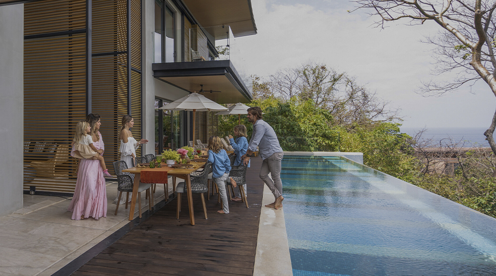 A family prepares to enjoy a meal on a patio with a private infinity pool and an ocean view