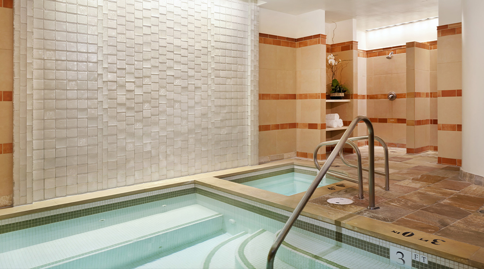 Corner of a rectangular indoor pool with a handrail and tiled floor