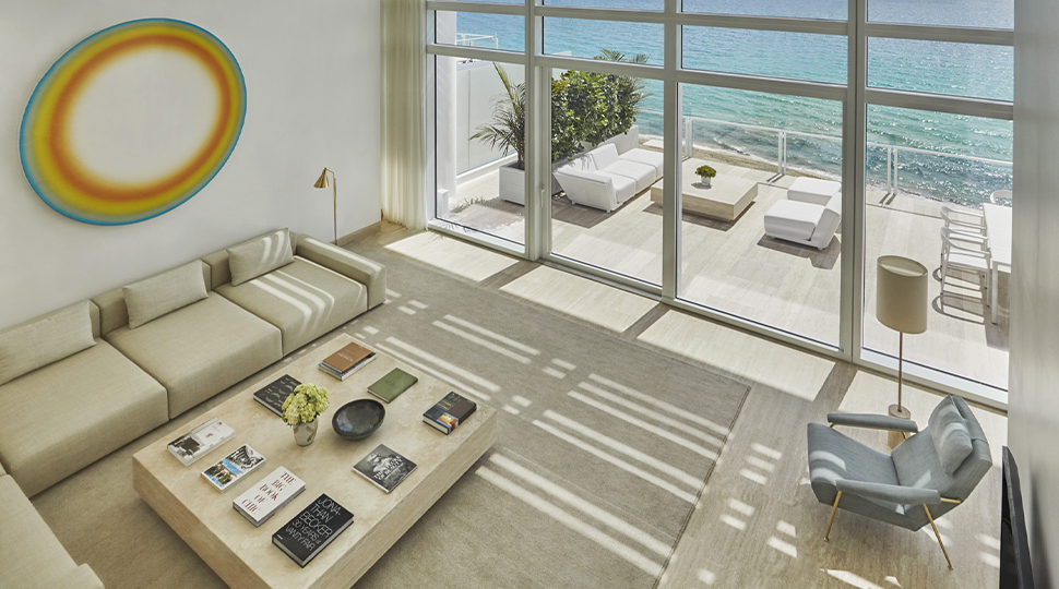 Looking down at bright living room with white L-shaped sofa, armchair, art, glass window wall