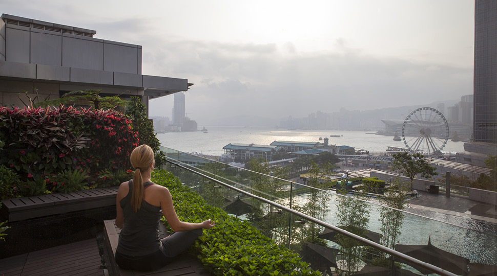 Woman mediating on a rooftop overlooking a harbour and ferris wheel