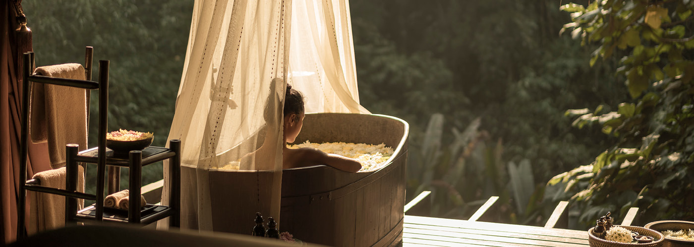 A woman lounges in a canopied bathtub overlooking the jungle