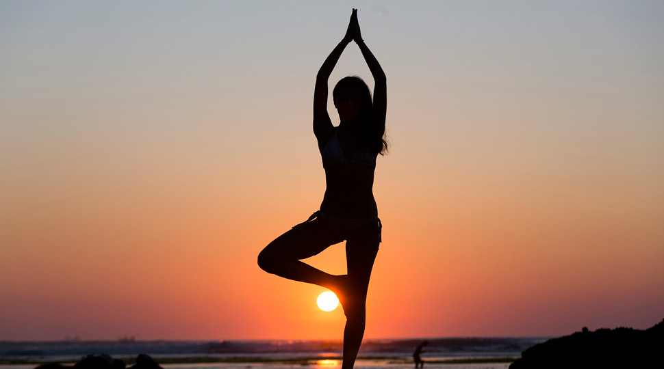 Silhouette of a woman holding a yoga pose overlooking the ocean and sunset