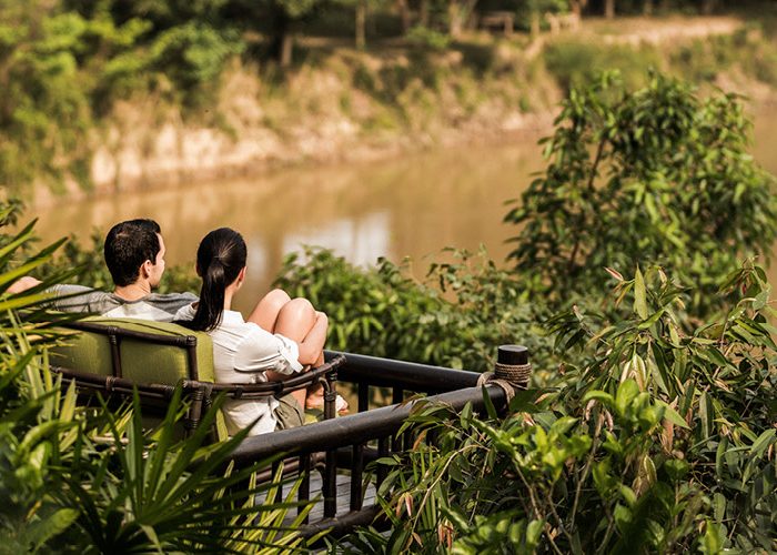 A couple sits on an outdoor couch overlooking the jungle