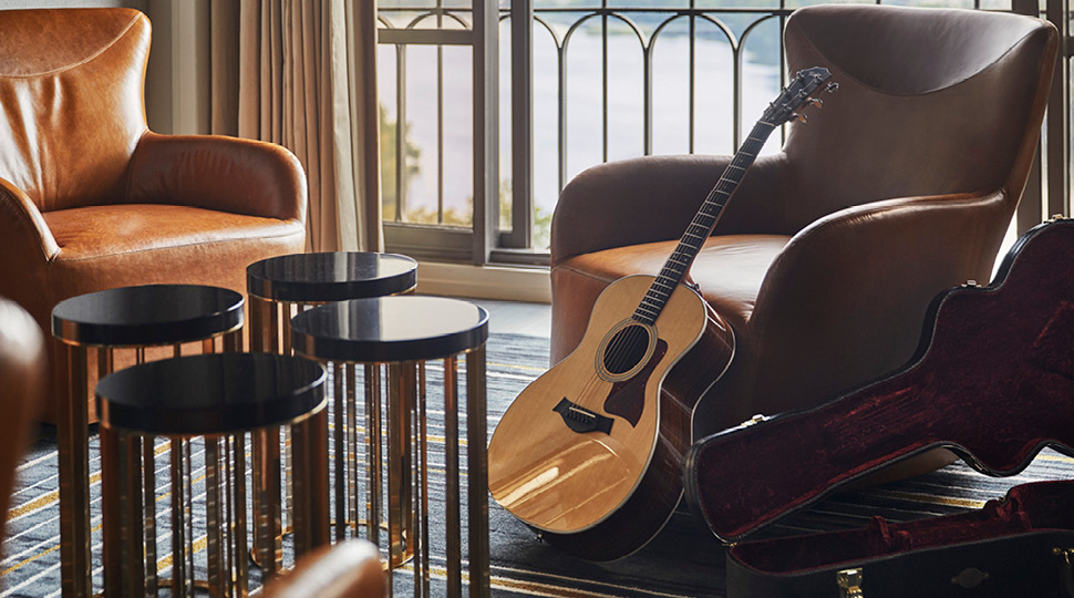 A guitar leans up against a brown leather chair by a balcony