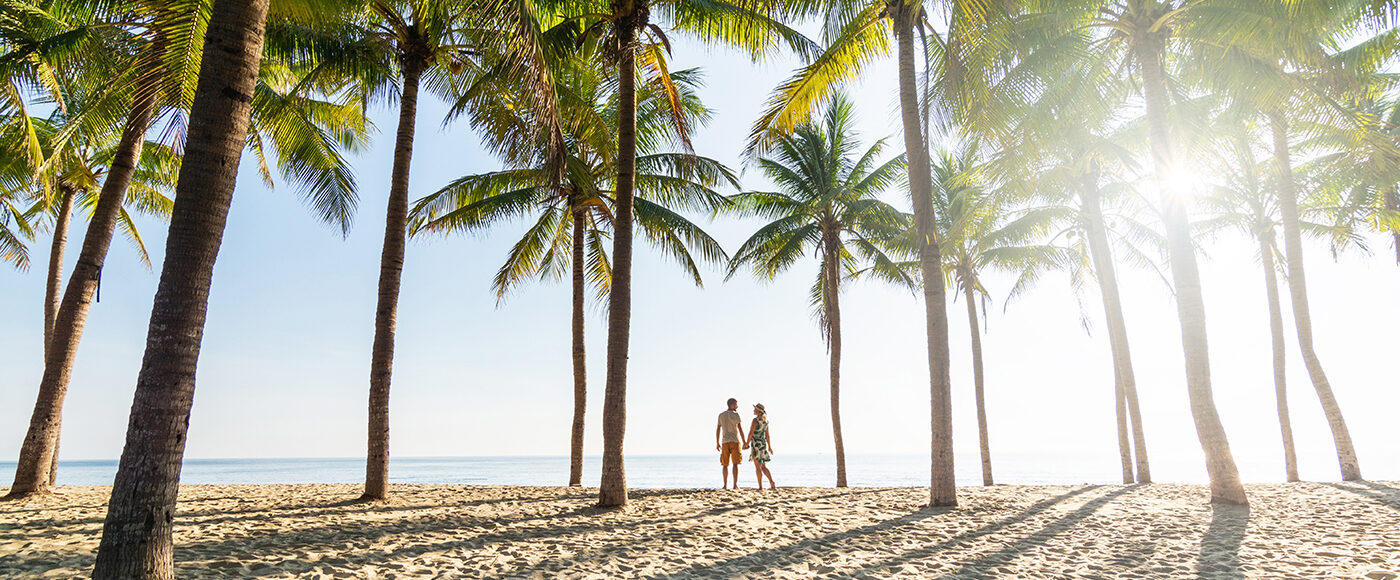 Couple Standing On Sandy Beach Among Palm Trees On Sunny Morning
