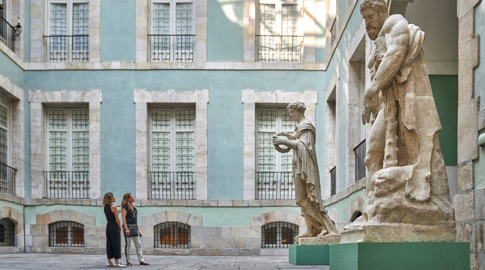 Two women in a courtyard looking up at two large marble sculptures