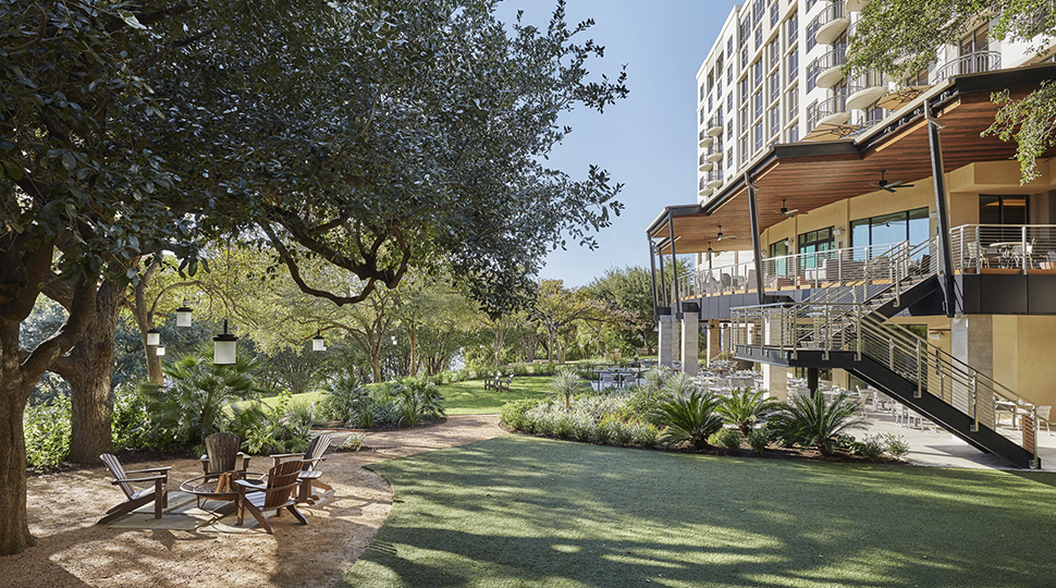 Outdoor lawn of Four Seasons Hotel Austin with a group of Adirondack chairs beneath the shade of a large tree