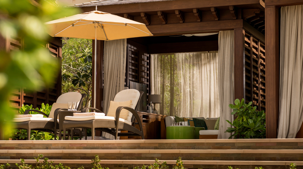 Two lounge chairs and a patio umbrella are set in front of a private pool cabana