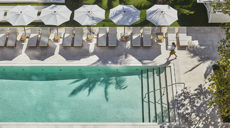 Aerial view of rectangular outdoor pool with a row of white lounge chairs and umbrellas along one side