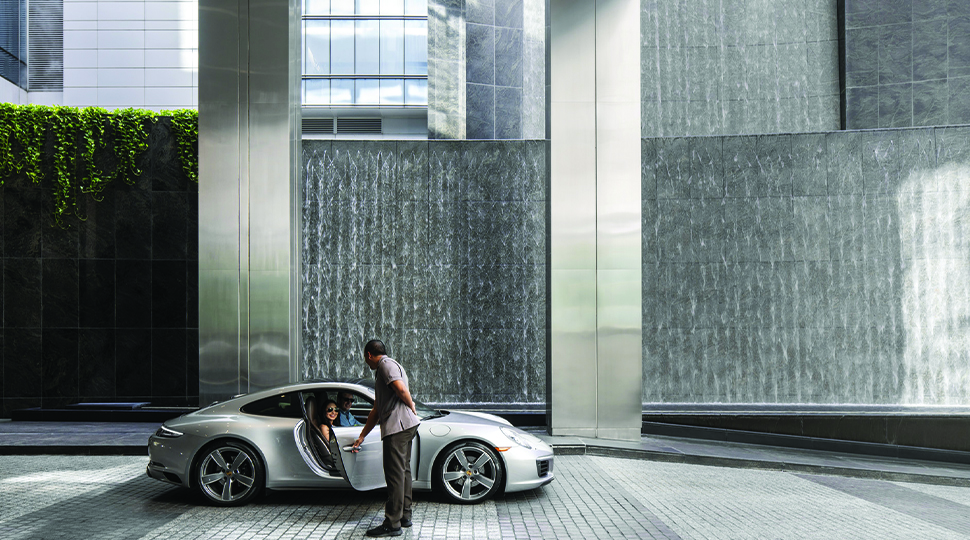 Valet opens door of silver sports car in front of a stone entrance