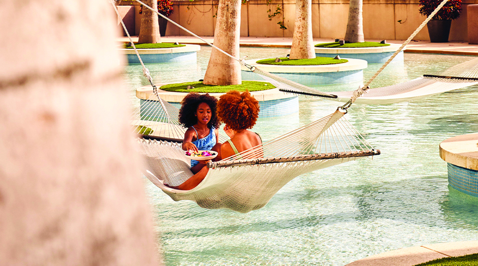 Two young girls sitting in a hammock over a pool