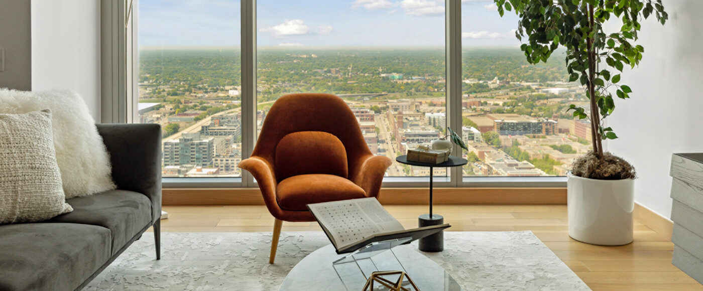A spacious living area decorated with colourful, modern furniture, an artificial plant, and a wall-to-wall window overlooking a Minneapolis city view