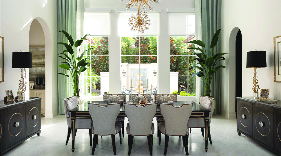 Dining room with extra-tall ceilings, large windows, green curtains and two buffets on either side of a dining table set for 8