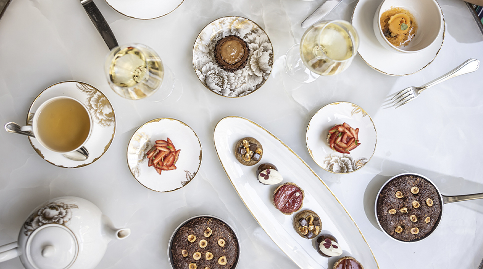 Overhead view of a table filled with small gold-rimmed plates of food and a white ceramic tea set for two