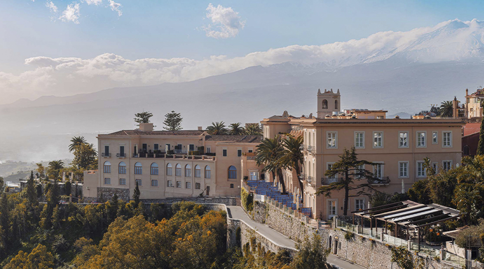 Exterior view of historic hotel on a hillside in Sicily with cloud-covered mountains in the distance