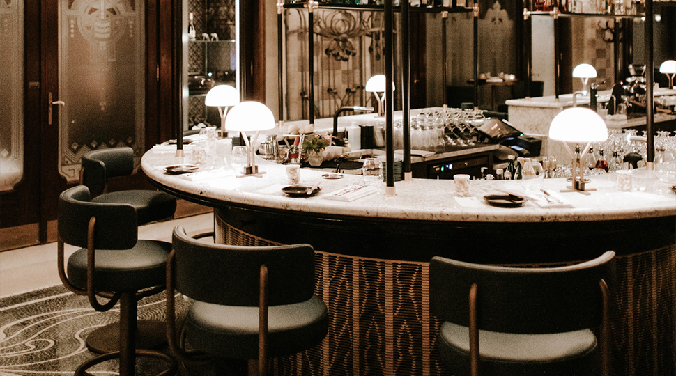 White marble-top bar with leather curved back stools and small round lamps at MÚZSA in Budapest