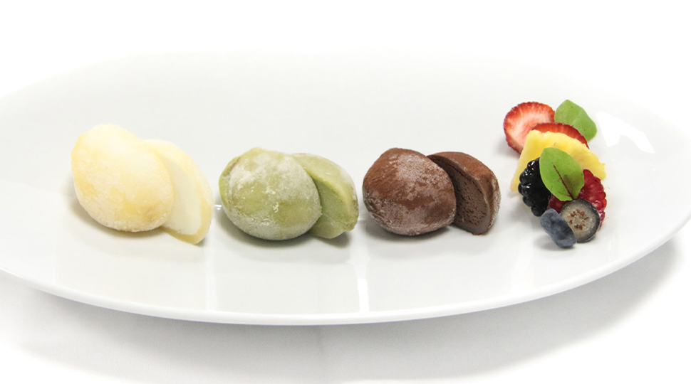 Three scoops of mochi ice cream in yuzu, matcha and chocolate plated on a white oblong dish with fresh strawberries, pineapple and berries on the side