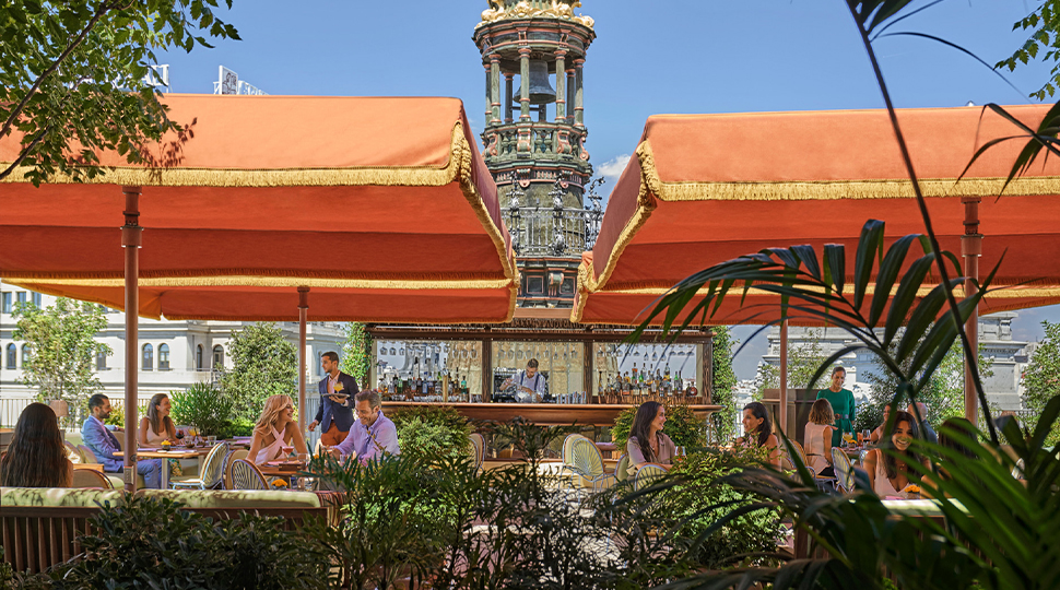 Open-air restaurant dining patio with very large orange shade umbrellas surrounded greenery and city views of Madrid