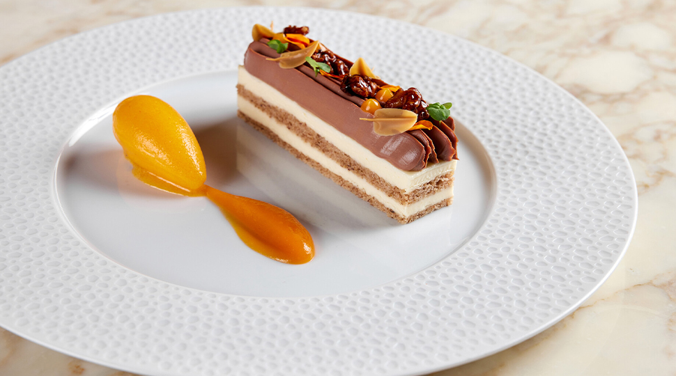 Five-layered walnut cheesecake and scoop of nutmeg sorbet is served on a round white dish