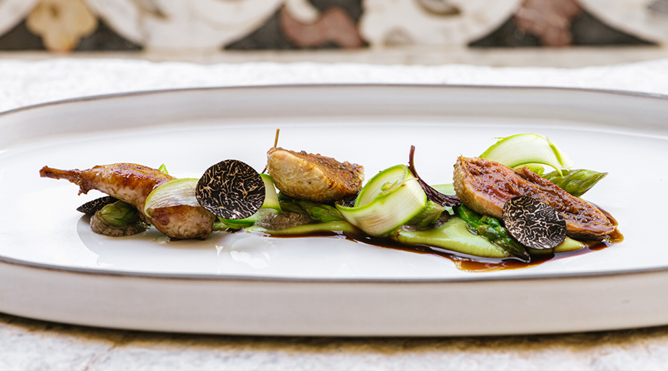 Close up image of quail, green asparagus and black truffle slices on a white dish served at Principe Cerami in Taormina