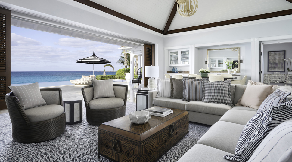 Living room furnished in a light-grey and white colour palette opens up to a large outdoor terrace with the ocean in the distance