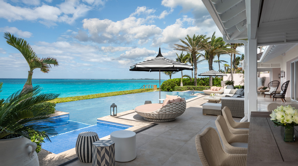 Outdoor terrace furnished with various lounge seating, an umbrella and a rectangular infinity pool overlooking the ocean