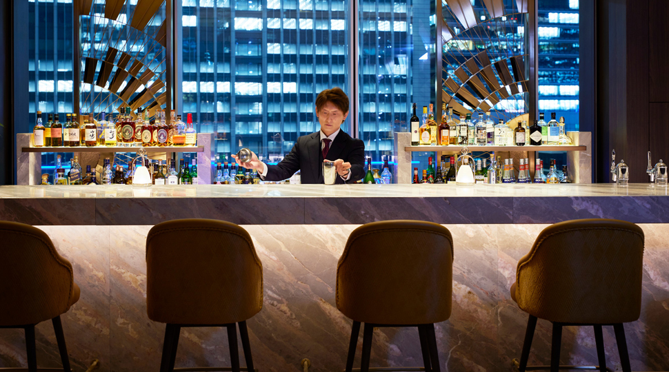 Bartender mixes drinks behind the counter with a city skyline in the background