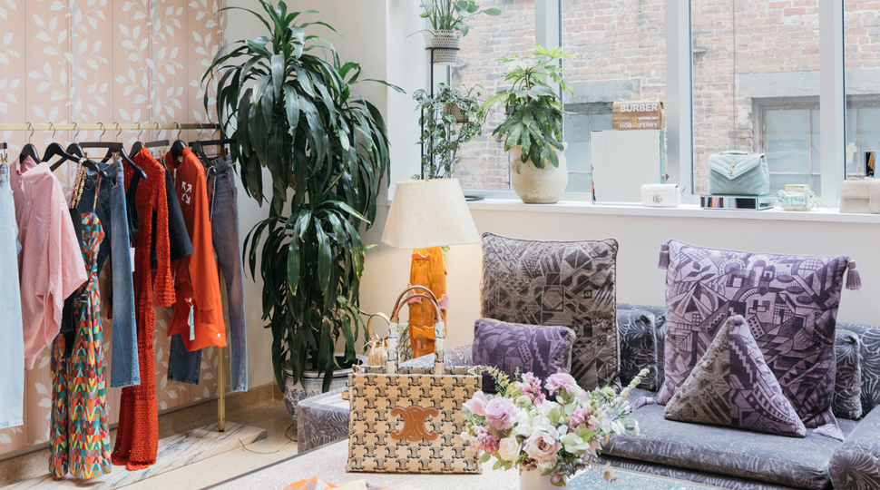 A rack of clothing, violet couch and various plants fill a brightly lit fitting room