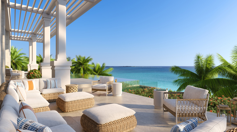 Private outdoor patio furnished with rattan lounge furniture that looks out onto the ocean and palm trees