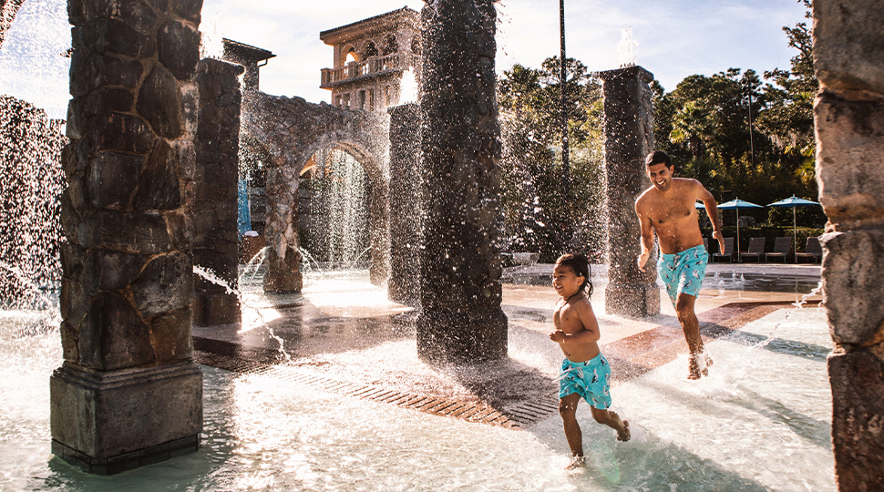 A father and son run through a splash pad