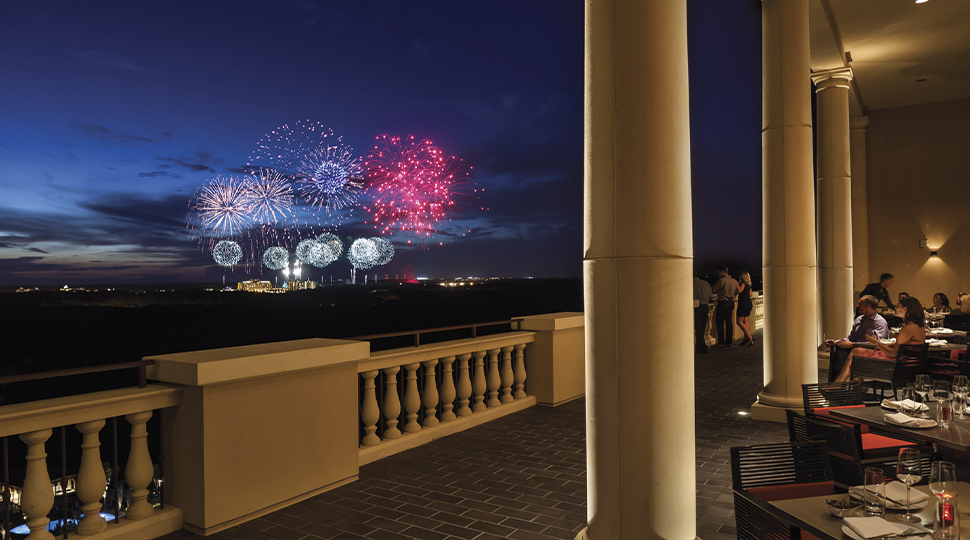 Fireworks going off in the distance as people dine on a rooftop terrace