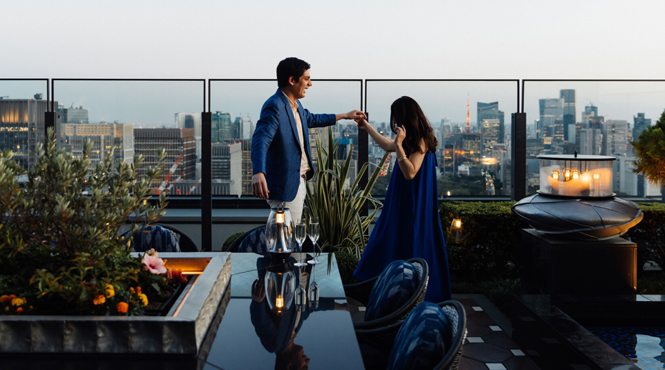 A couple dances on a rooftop patio with the city skyline in the distance