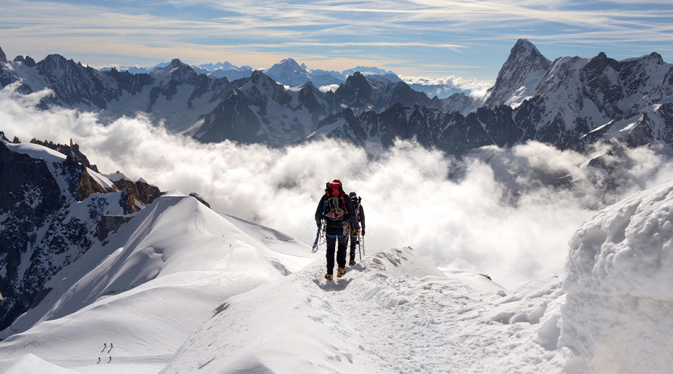 Two people hiking along the ridge of a snow-covered mountain