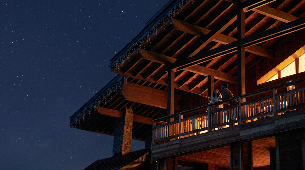 Two people standing on the terrace of a mountain-top lodge at night