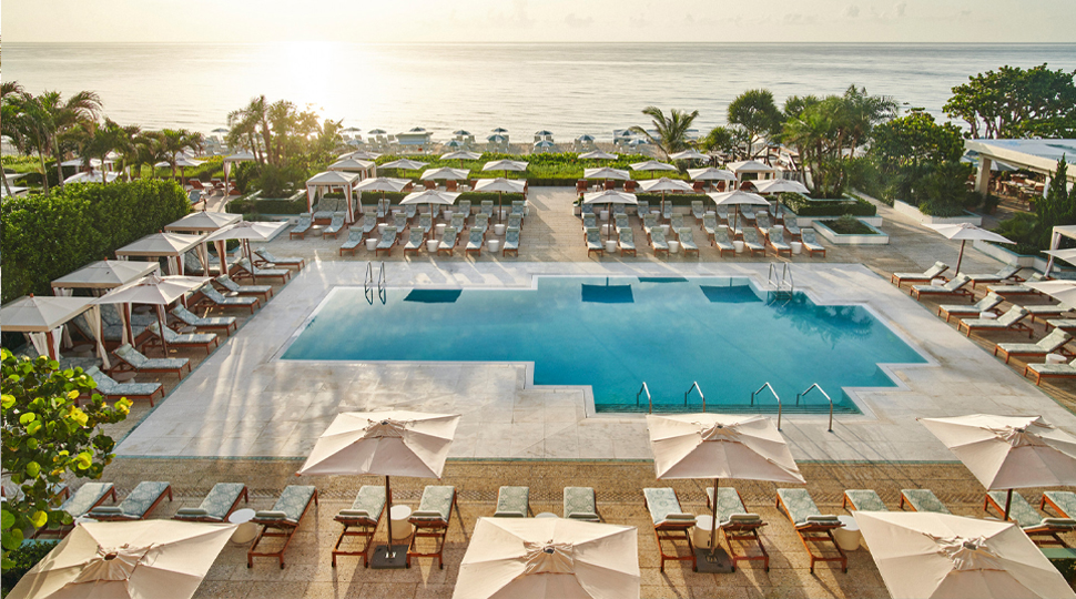 Aerial view of outdoor pool surrounded by rows of lounge chairs with the ocean in the distance