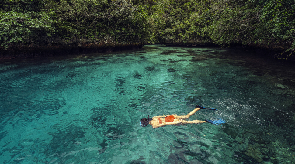 Person wearing red two-piece bathing suit snorkels through a turquoise lagoon