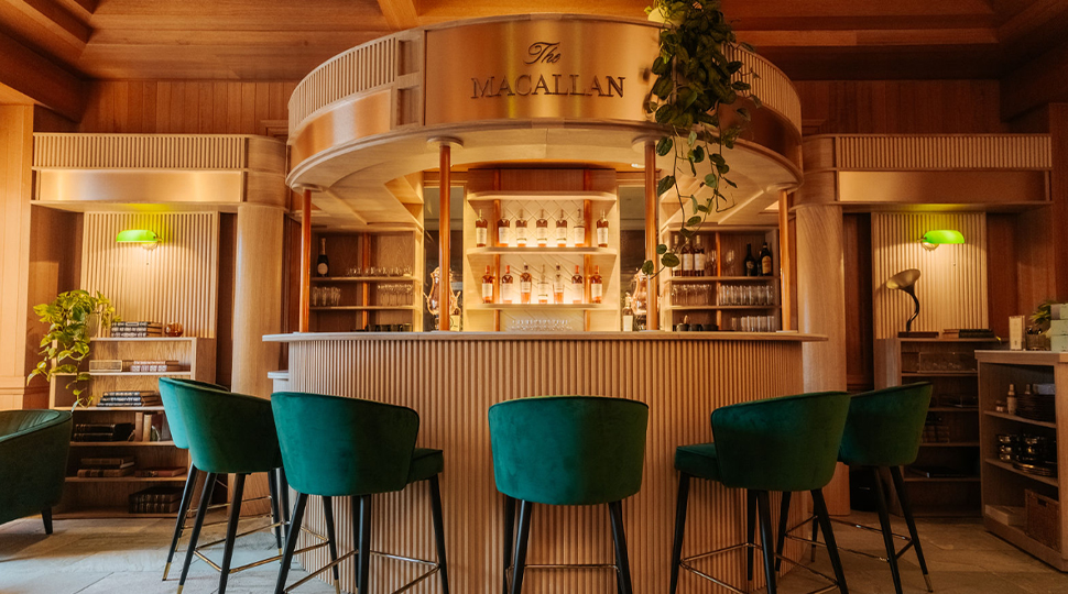 Five green velvet bar stools surround a light-wood curved bar