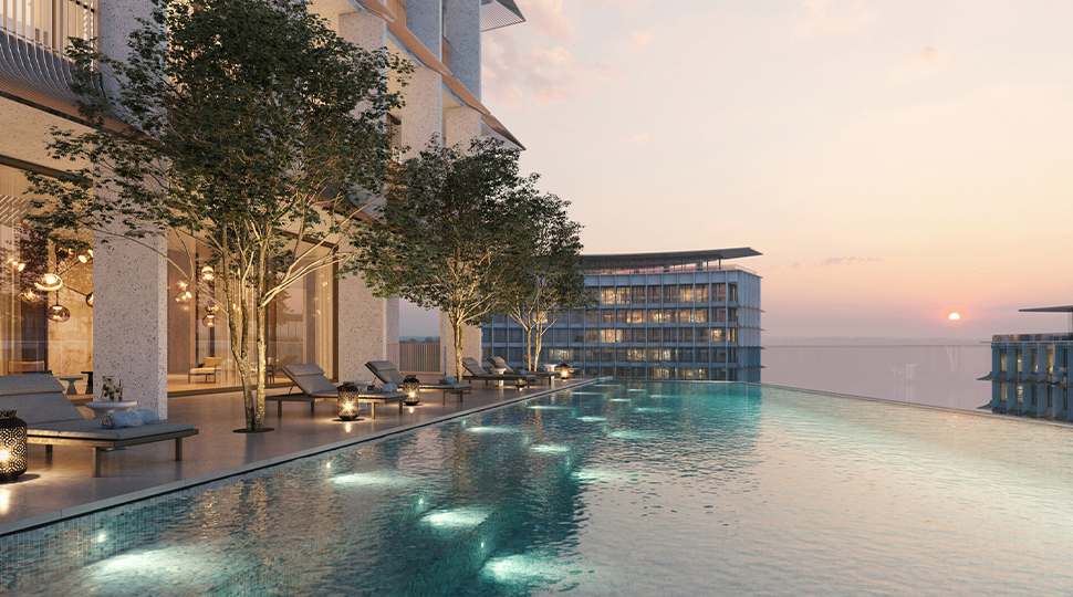 Rooftop infinity-edge pool reaches out to the skyline with a row of lounge chairs and three small trees along the side