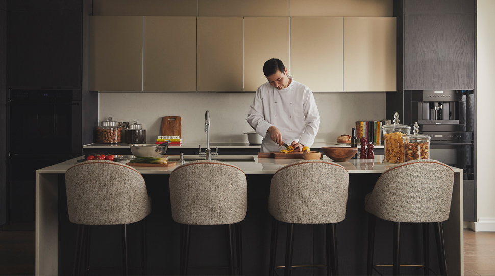 Chef wearing white chef's jacket stands behind a waterfall-style kitchen island slicing oranges