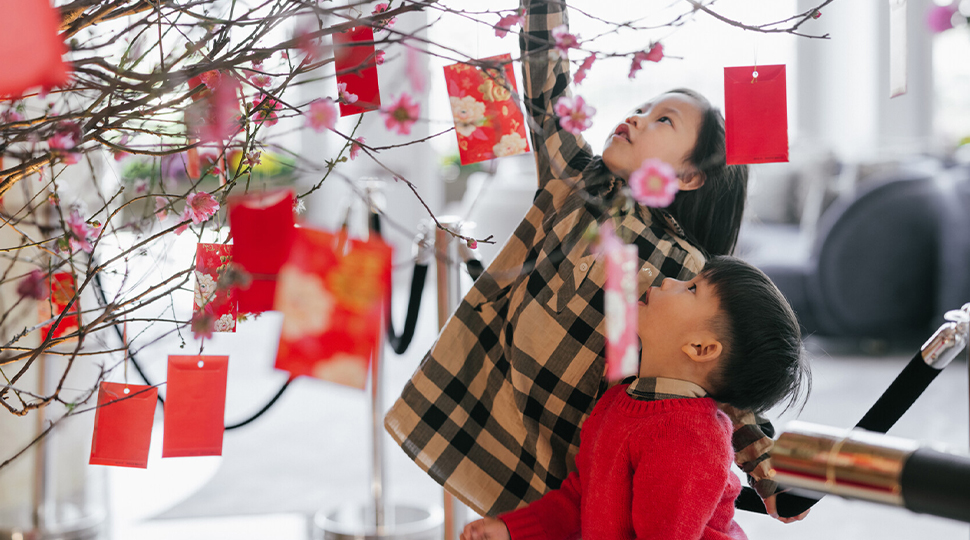 Two children dressed in winter clothing look at red card hanging from tree branches